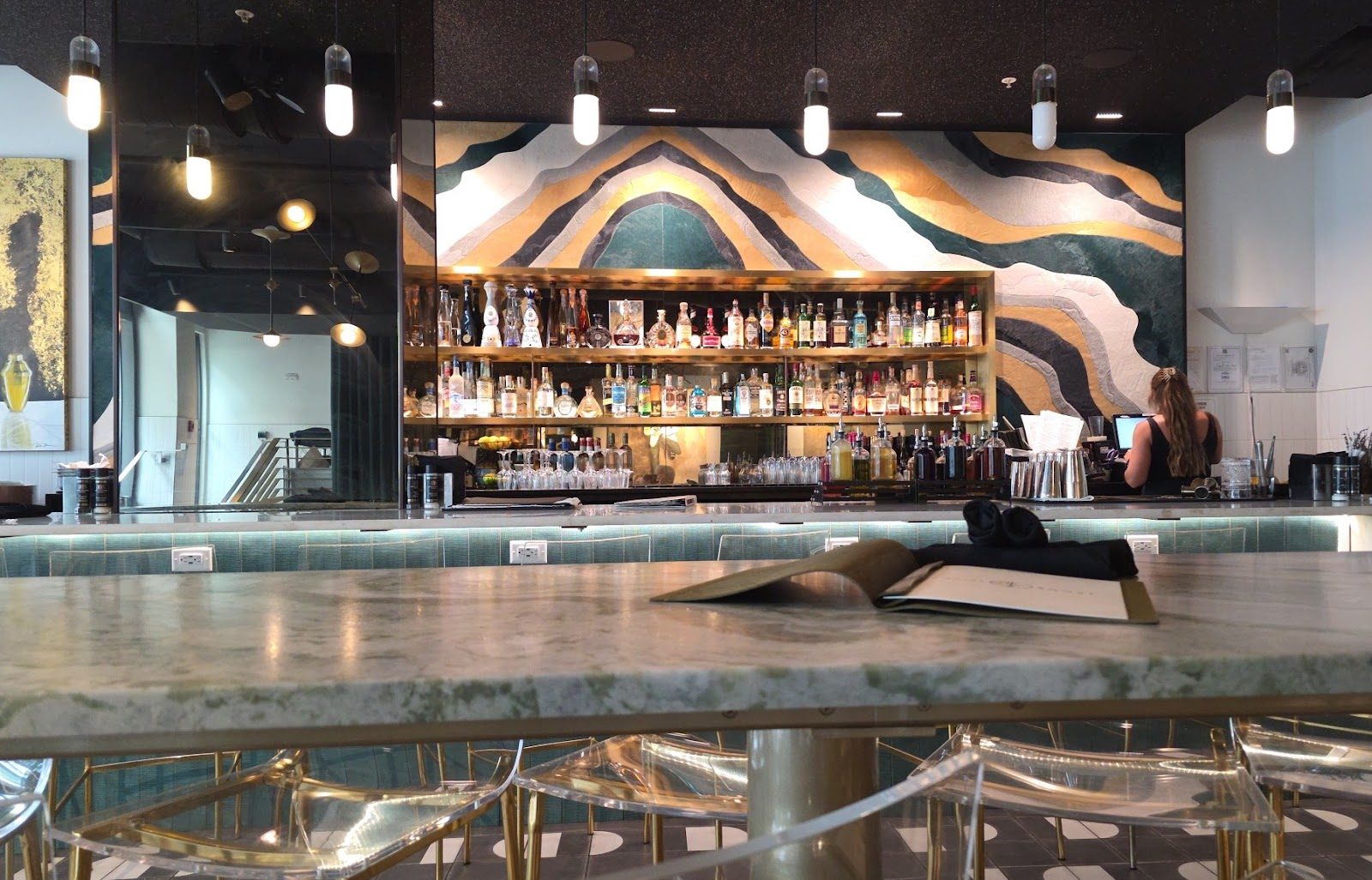 A sculptural, backlit wavy-wood wall rising behind the marble bar.