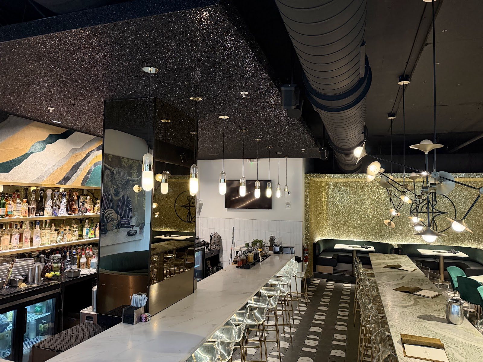 The long marble bar with green banquettes, bar stools and pendant lights.