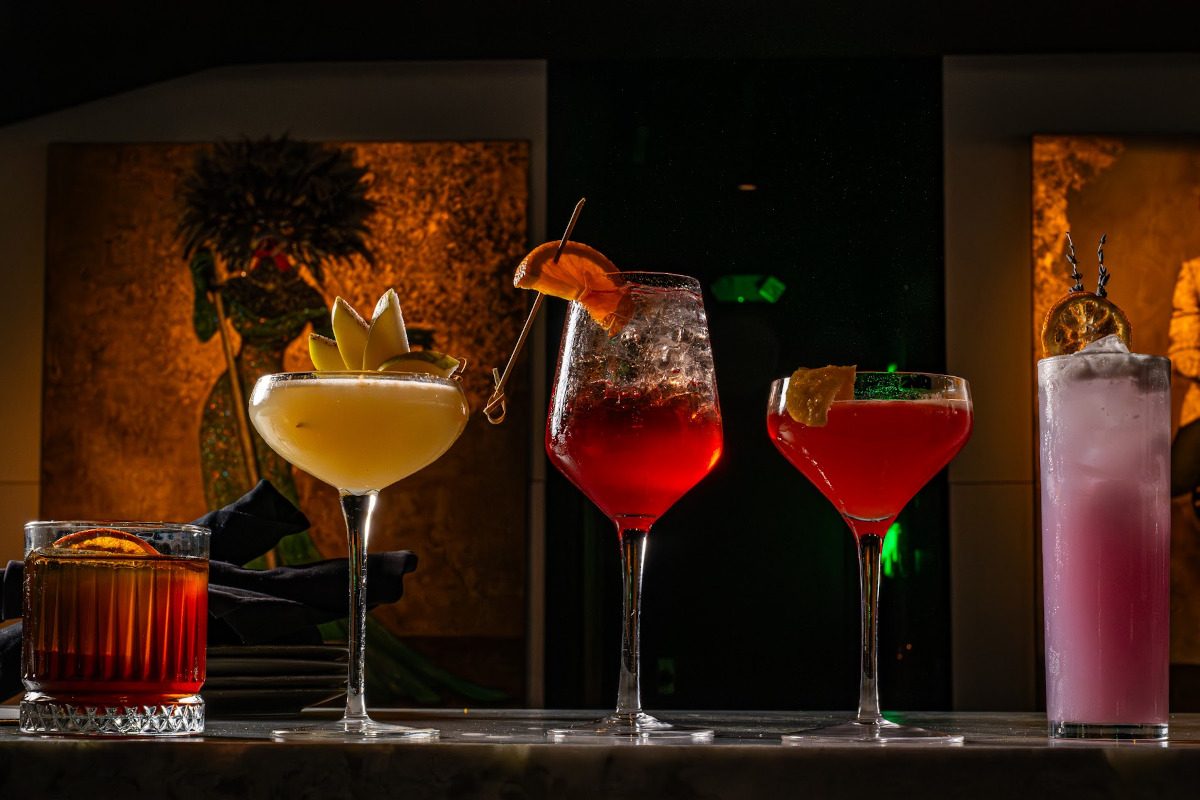 Four craft cocktails lined up on the marble bar against a dark, moody backdrop.