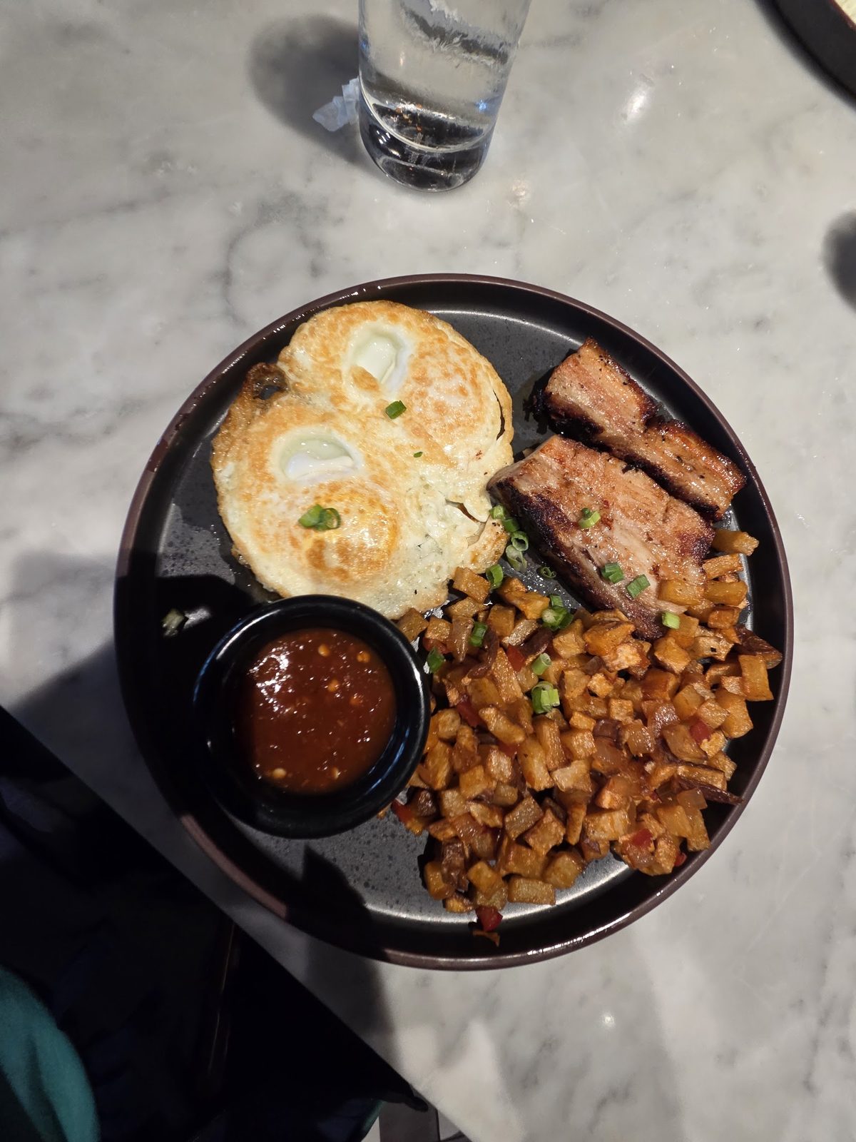 A brunch plate with a biscuit, seasoned potatoes and a ramekin of chili relish.