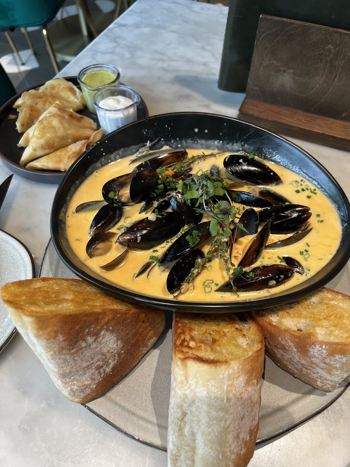A bowl of mussels in golden curry broth, ringed with toasted ciabatta.