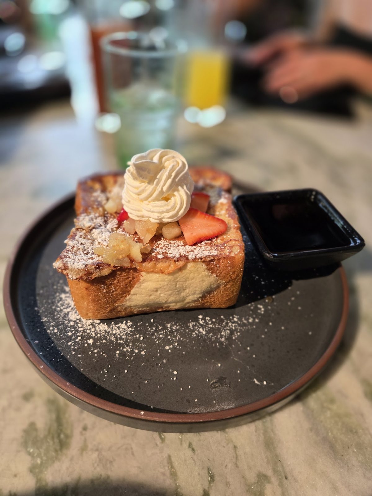 Stuffed French toast dusted with sugar, with strawberries, cream and a dish of syrup.
