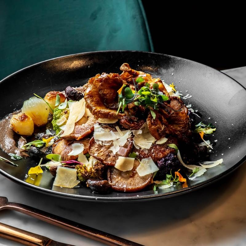 A dark plate of braised short rib with shaved vegetables, herbs and flowers.